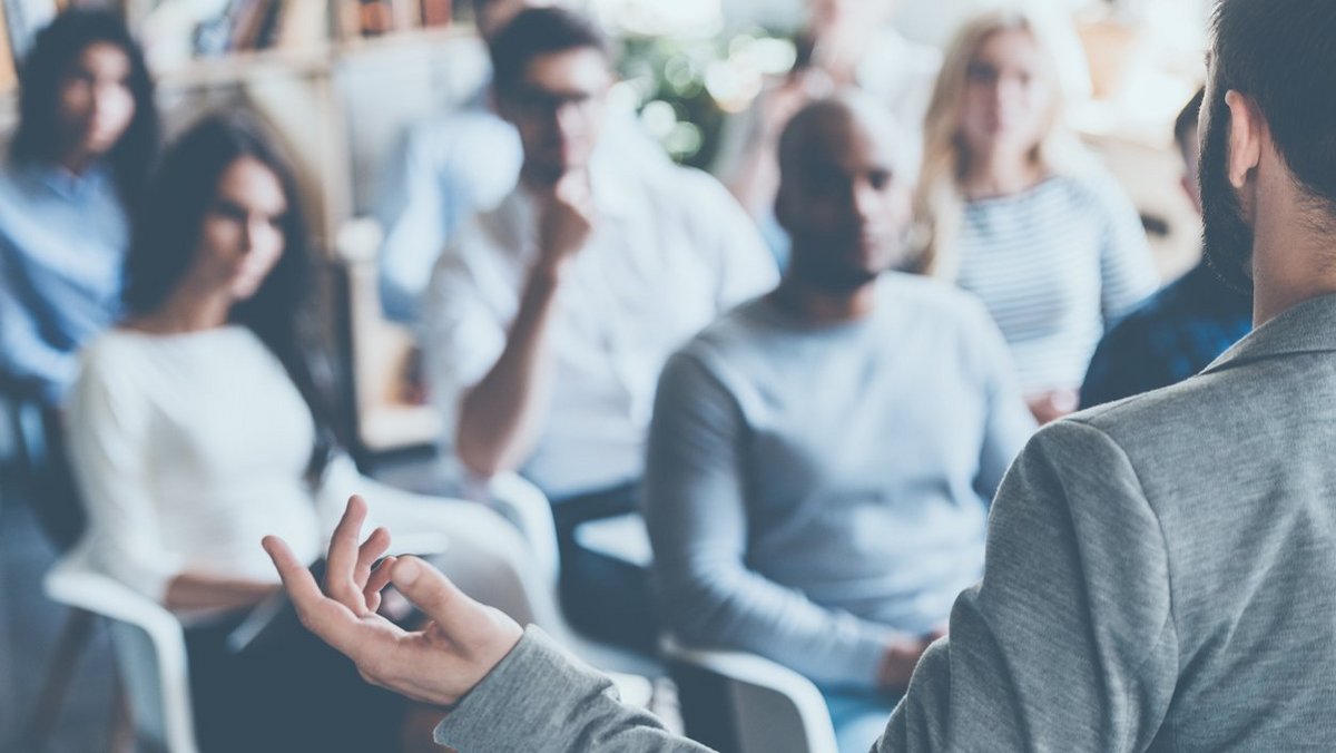 Mann referiert vor Menschenmenge