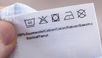 Hand hält weißes Textiletikett mit verschiedenen Pflegehinweisen