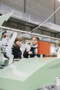Die Yarn Sustain Gründerinnen Franziska Uhl und Ann Cathrin Schönrock stehen in der Maschinenhalle der Hochschule Reutlingen.
